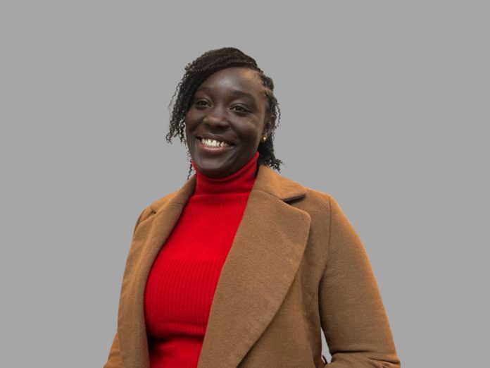 A picture of Josephine Badu-Nyarko the author of the article. A picture of a smiling young Ghanaian woman wearing an orange dress with a brown jacket typically work in cold weather